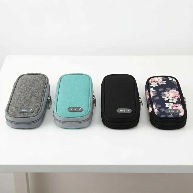 Trousses isothermes rectangulaires en tissu, présentées en quatre coloris : gris, vert, noir et motif floral, posées sur une table blanche.