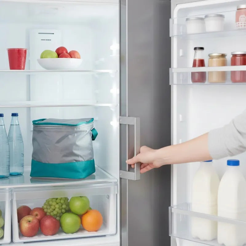 Sac isotherme gris et turquoise posé dans un réfrigérateur, à côté de bouteilles d’eau.