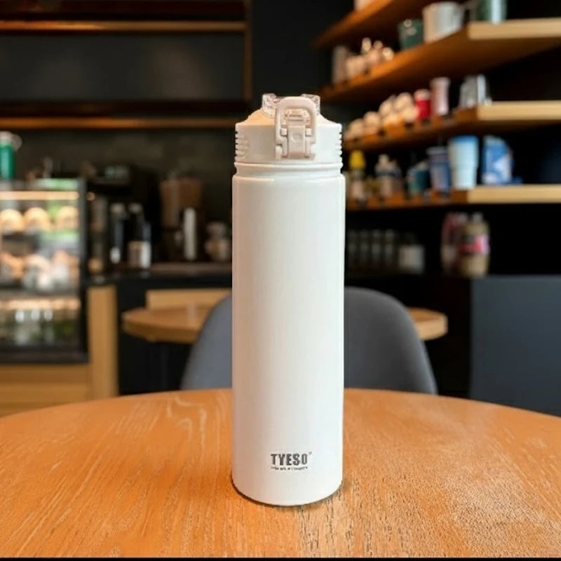 Bouteille isotherme en inox blanc TYESO posée sur une table de café, avec bouchon sport anti-fuite et design épuré, idéale pour garder les boissons chaudes ou froides plusieurs heures.