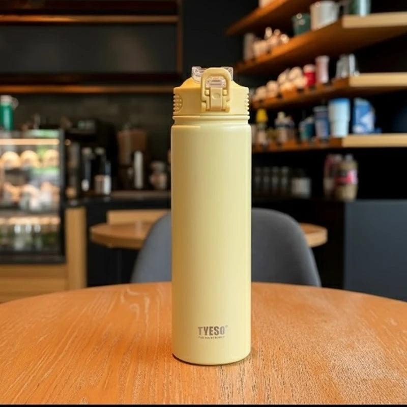 Bouteille isotherme en inox jaune TYESO posée sur une table de café, avec bouchon sport anti-fuite et design élégant, idéale pour garder les boissons chaudes ou froides plusieurs heures. 