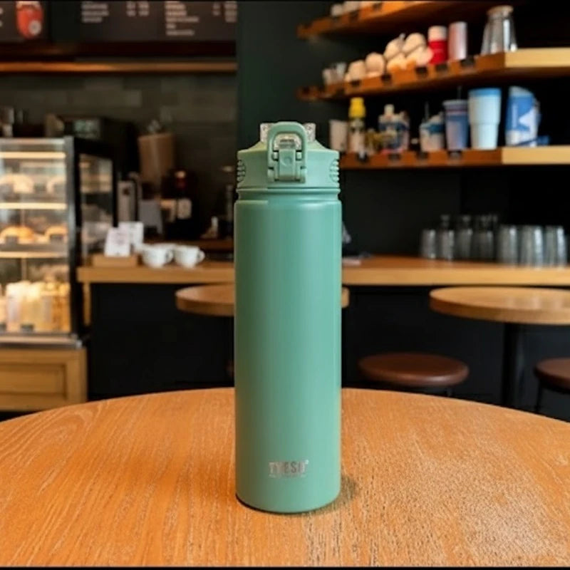 Bouteille isotherme en inox vert TYESO posée sur une table de café, bouchon sport anti-fuite, design moderne et minimaliste, idéale pour garder les boissons chaudes ou froides plusieurs heures.