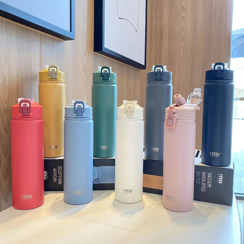 Ensemble de bouteilles isothermes en inox TYESO présentées sur un comptoir en bois, disponibles en plusieurs couleurs pastel et mates — rouge, jaune, vert, gris, bleu, blanc et rose — avec bouchon sport anti-fuite et design moderne.