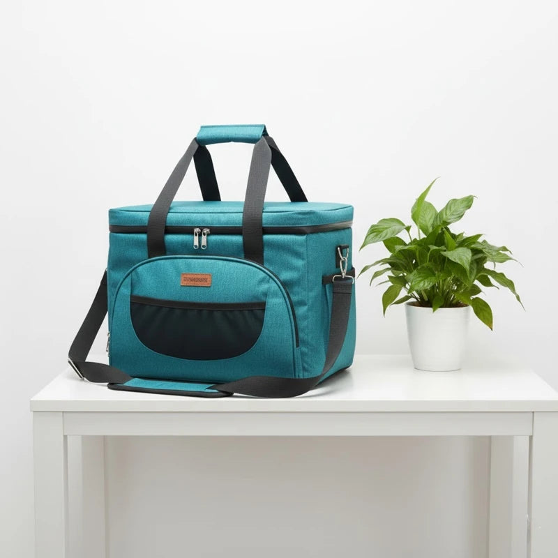 Glacière isotherme bleu azur vue de biais, posée sur une table blanche, avec grande poche frontale et bandoulière renforcée pour transporter repas et boissons.