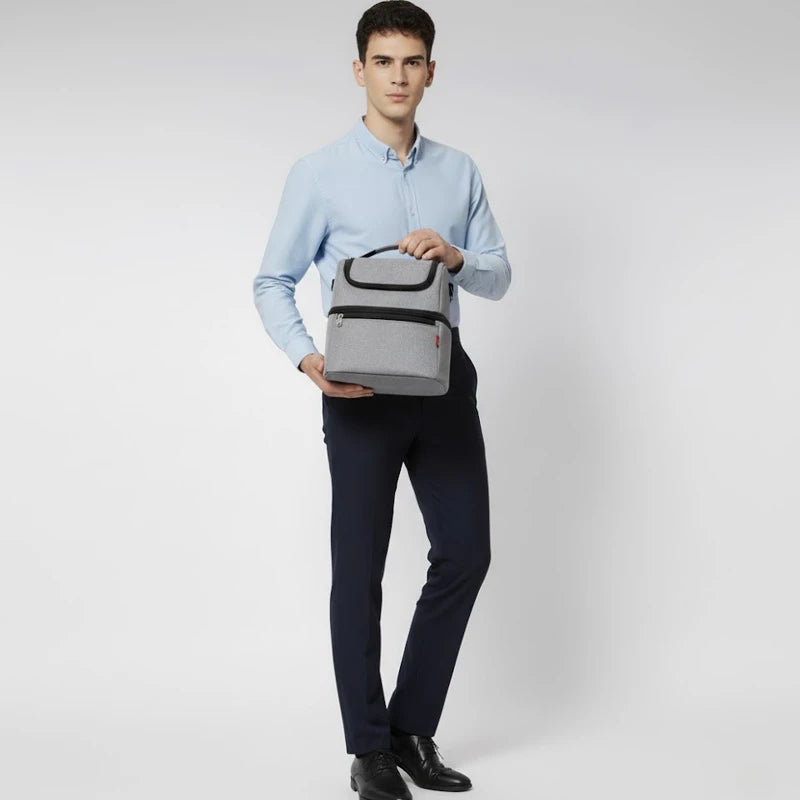 Homme debout tenant un sac isotherme gris par la poignée, en chemise bleue et pantalon foncé