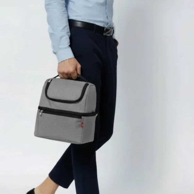 Main d’un homme tenant un sac isotherme gris en marchant, cadrage sur le bas du corps.