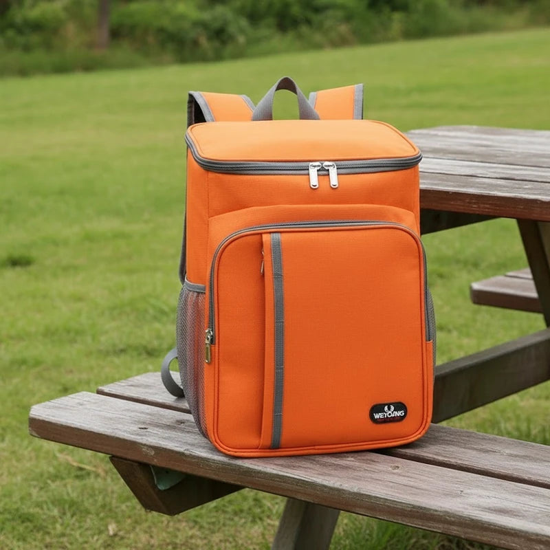 Sac à dos isotherme orange posé sur un banc en bois dans un parc verdoyant, illustrant un usage pratique pour les pique-niques et les sorties en plein air.