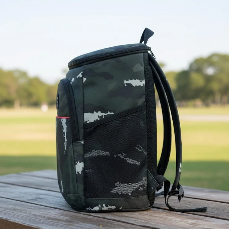 sac à dos isotherme camouflage vert posé sur un banc en bois, vue latérale avec poche filet visible