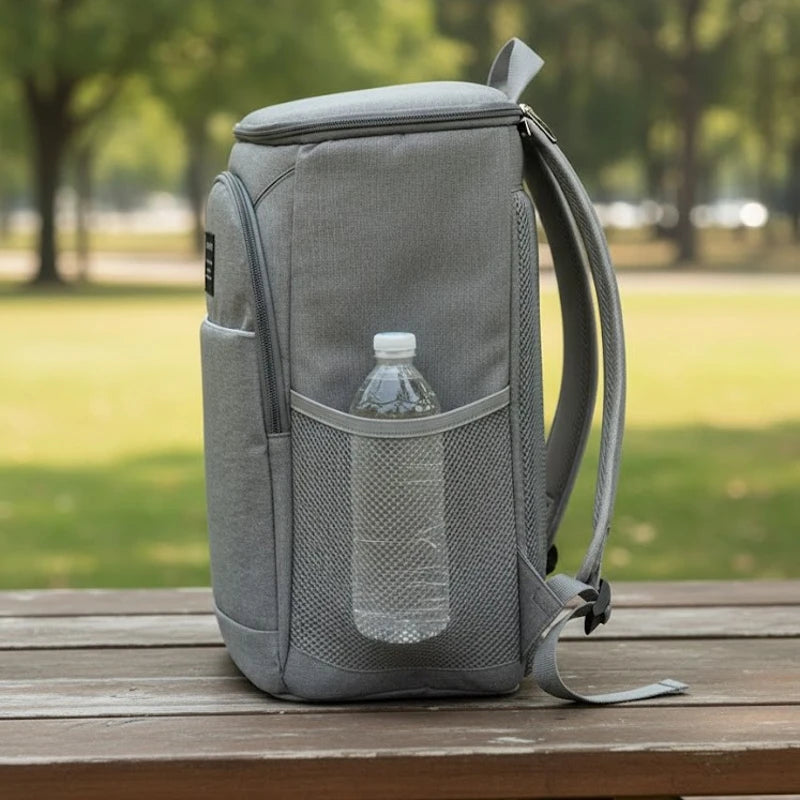 sac à dos isotherme gris posé sur une table, vu de côté avec poche filet contenant une bouteille d’eau
