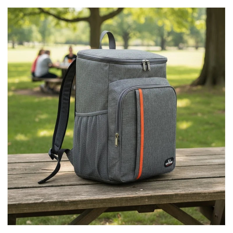 Sac à dos isotherme gris posé sur une table de pique-nique dans un parc, vu de côté, avec poche filet et détails orange.