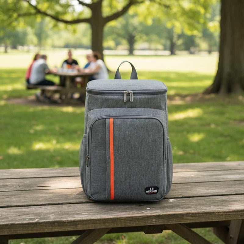 Sac à dos isotherme gris posé sur une table de parc en bois, avec un fond de pelouse et d’arbres, idéal pour pique-nique et repas au frais.