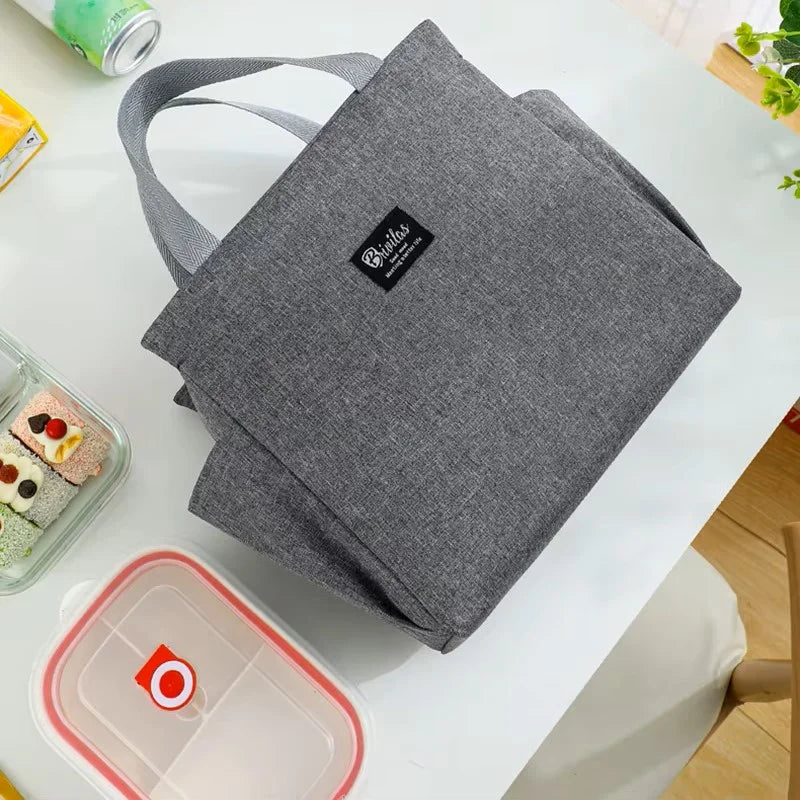 Sac isotherme repas gris vu de dessus, avec poignées en tissu et structure souple, posé sur une table avec boîtes alimentaires et encas, conçu pour transporter un déjeuner ou un repas du midi.