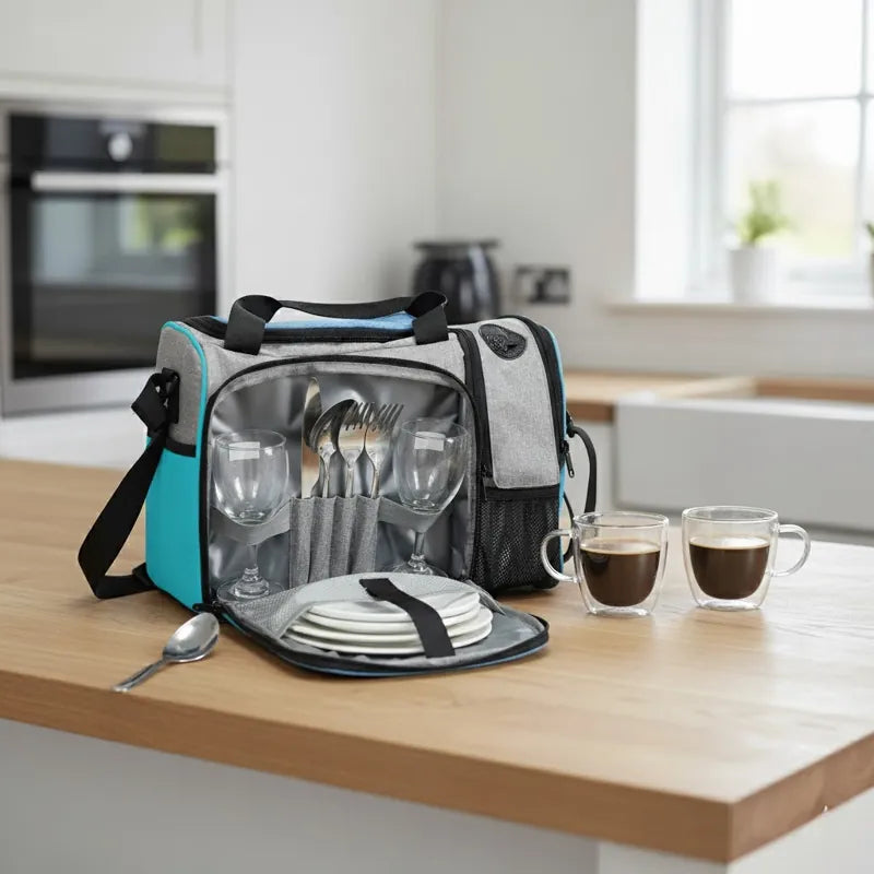 Sac isotherme 25L gris et bleu turquoise ouvert sur une table, contenant des verres, assiettes et couverts, idéal pour repas et pique-niques élégants.