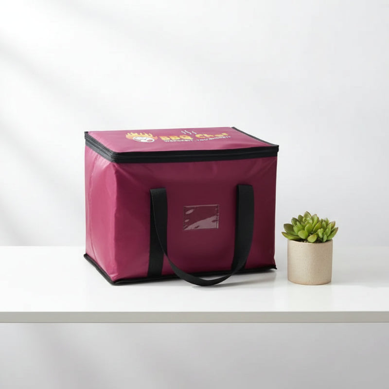 Sac isotherme bordeaux BBQ Chef vu de face, posé sur une table blanche, avec poignées noires et logo imprimé sur le dessus.