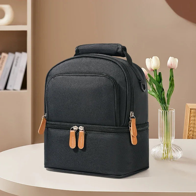 Sac isotherme bébé noir à double compartiment, conçu pour transporter biberon et accessoires, posé sur une table dans un intérieur sobre et lumineux.