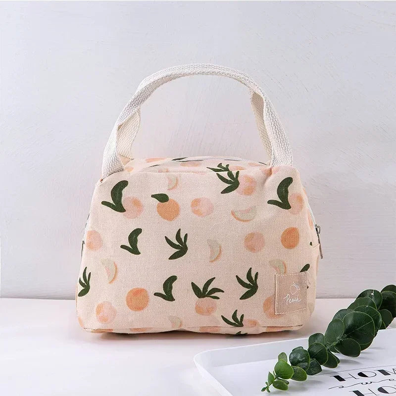 Sac isotherme beige à motifs pêches et feuilles vertes, vu de face sur une table blanche, avec anses en coton tressé et fond clair minimaliste.