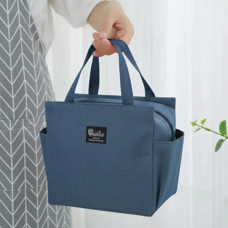 Sac isotherme bleu porté à la main, type lunch bag, tenu par une personne en intérieur