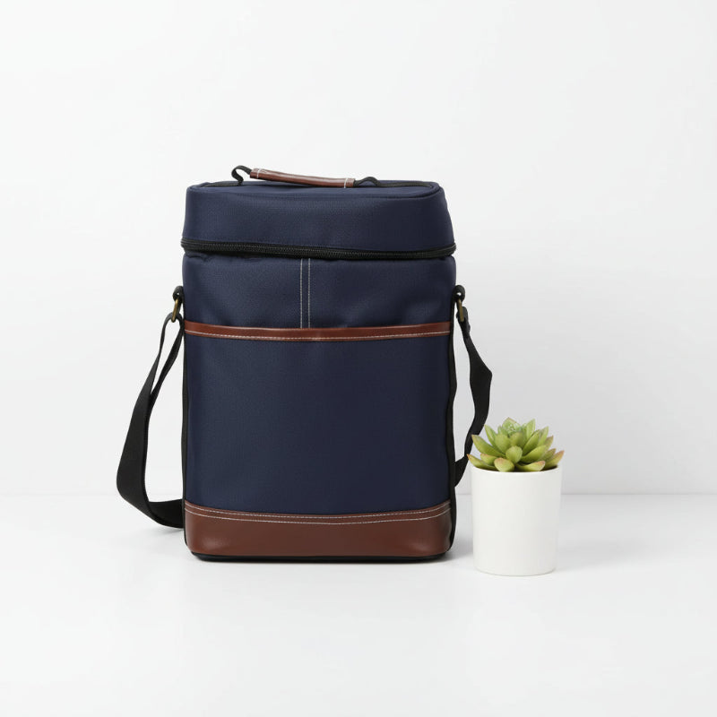 Sac isotherme pour bouteille bleu marine avec finitions cuir marron, présenté debout sur une table avec une petite plante décorative.