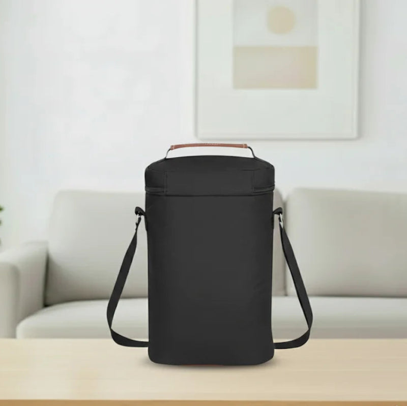 Vue arrière d’un sac isotherme bouteille noir avec bandoulière réglable et poignée en cuir marron, posé sur une table en bois clair dans un salon lumineux.