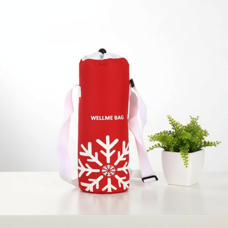 Sac isotherme pour bouteille rouge avec motif flocon blanc et bandoulière, posé sur une table blanche à côté d’une plante verte.