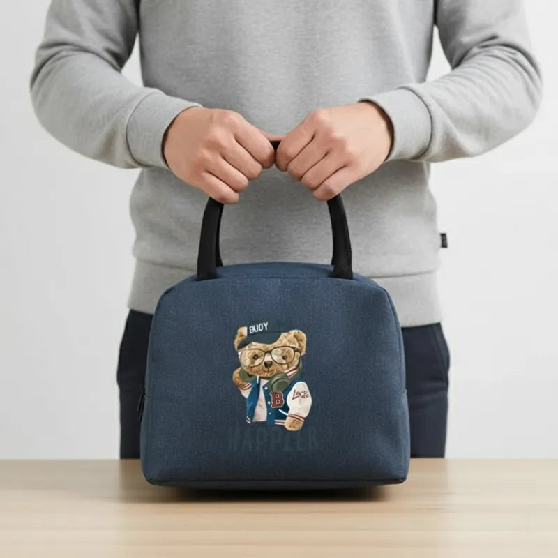 Sac isotherme enfant bleu motif ours Happier tenu à la main, posé en intérieur sur une table, vue lifestyle réaliste.