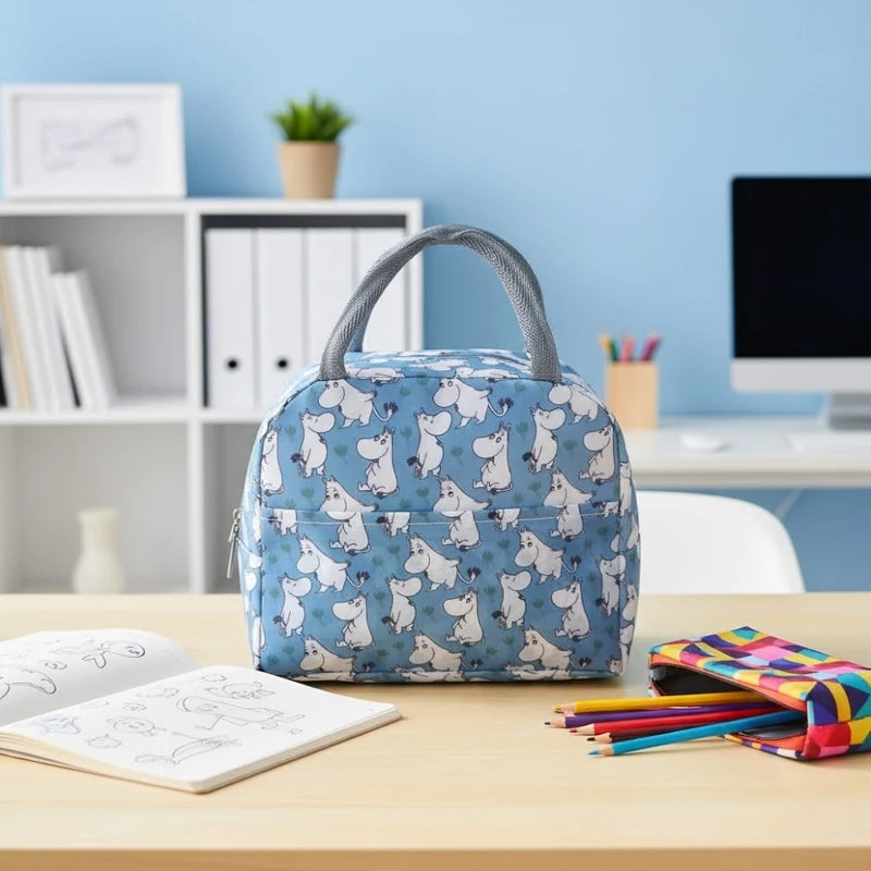 Sac isotherme enfant bleu avec motifs hippopotames posé sur un bureau d’école, à côté d’un cahier et de crayons.