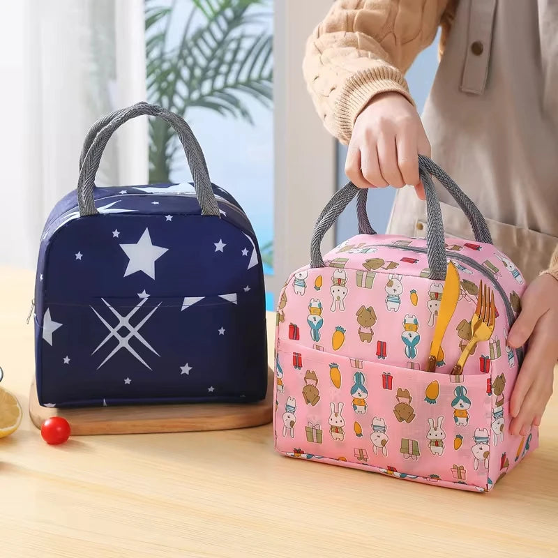 Deux sacs isothermes pour enfant, l’un bleu marine à motif étoiles et l’autre rose à motifs animaux, posés sur une table avec une main tenant le modèle rose.