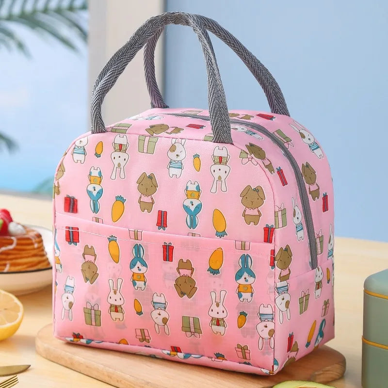 Sac isotherme pour enfant de couleur rose avec motifs de lapins et animaux, posé sur une table en cuisine.