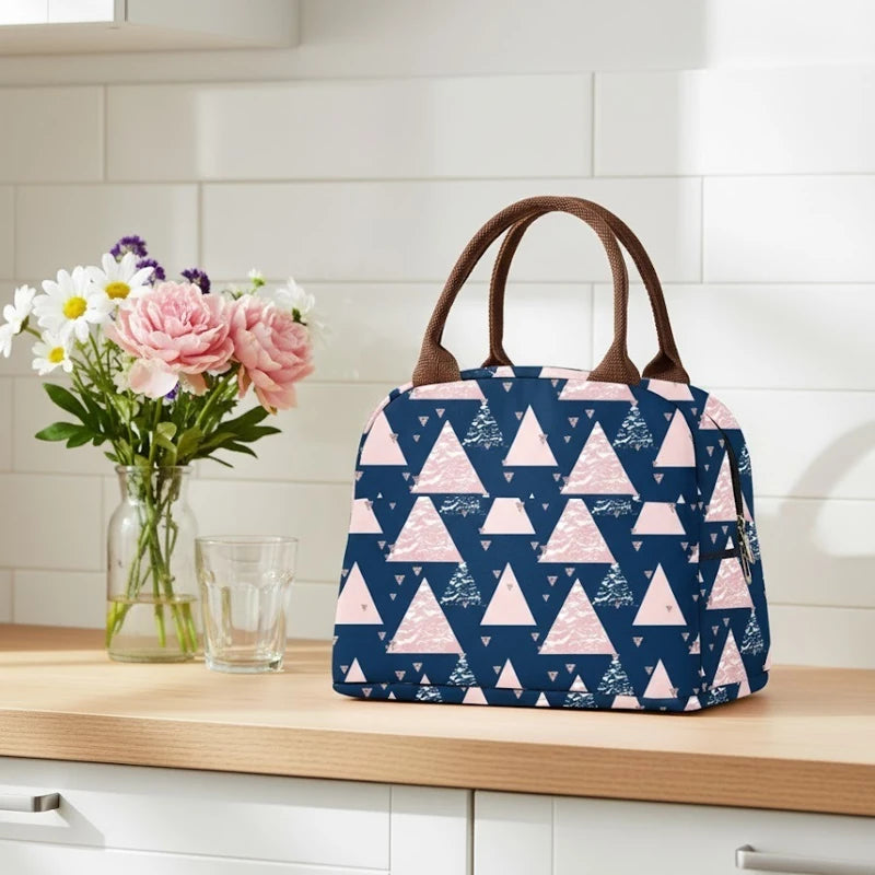 Sac isotherme bleu marine à motifs triangles roses posé sur un plan de travail en bois clair, à côté d’un vase de fleurs et d’un verre dans une cuisine lumineuse.