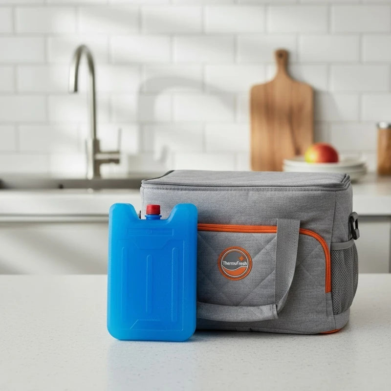 Sac isotherme gris avec poignée et fermeture orange, accompagné d’un pain de glace bleu posé sur un plan de travail de cuisine moderne.