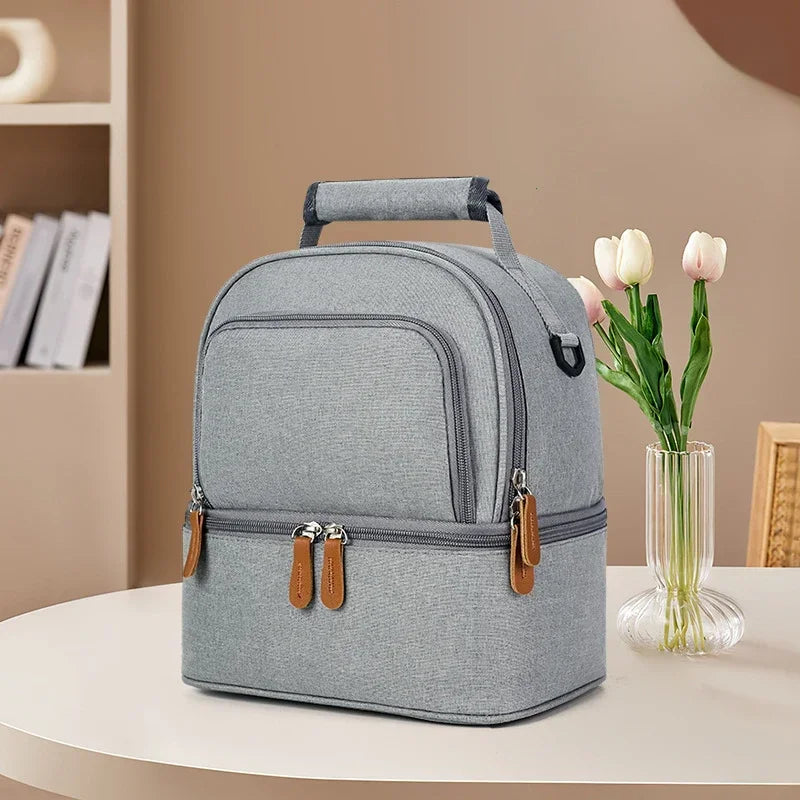 Sac isotherme gris à double compartiment posé sur une table, avec fermeture éclair et poignée renforcée.