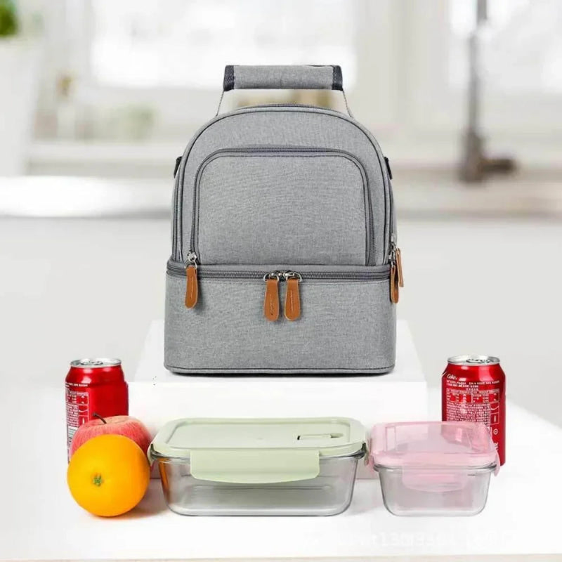 Sac isotherme gris posé sur une table avec boîtes repas, fruits et canettes autour.