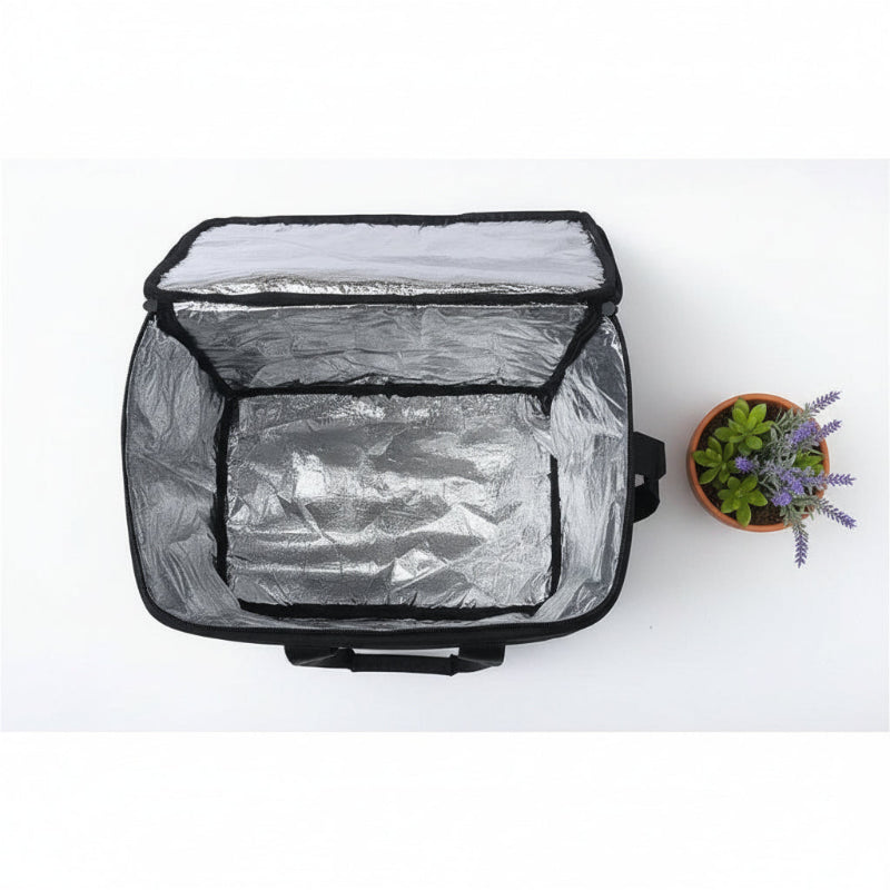 Intérieur aluminium d’un sac isotherme de livraison noir 50 L, ouvert et vu du dessus, posé sur une table blanche avec une plante décorative à droite.