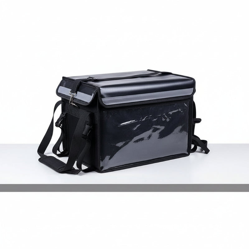 Sac isotherme noir à parois transparentes, vu de côté, avec rabat renforcé, sangles de maintien et bandoulière ajustable, conçu pour la livraison alimentaire poser sur une table blanche.