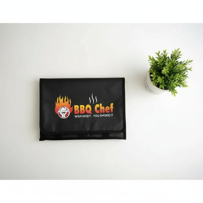Sac isotherme pliable noir BBQ Chef posé à plat sur une table blanche, avec une plante décorative à côté.