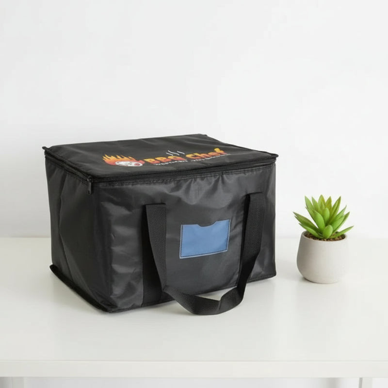Sac isotherme noir pour transport de repas, vu en angle, avec poignées renforcées et petite plante décorative sur table blanche.