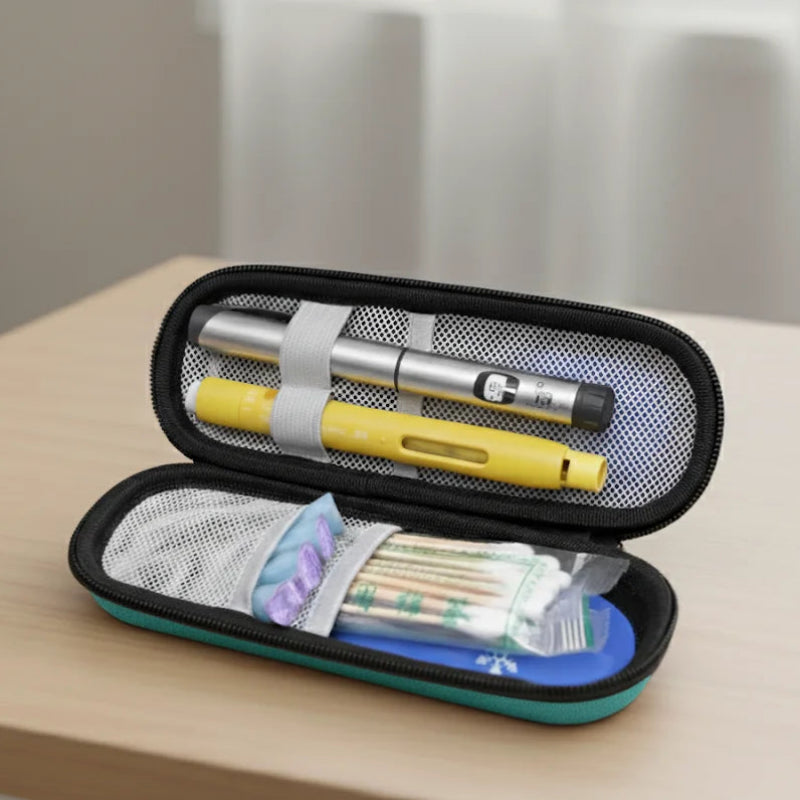 Étui isotherme médical vert ouvert, contenant deux stylos injecteurs d’insuline fixés par des sangles, ainsi que des accessoires de soins rangés dans des pochettes en filet, posé sur une table en bois clair.