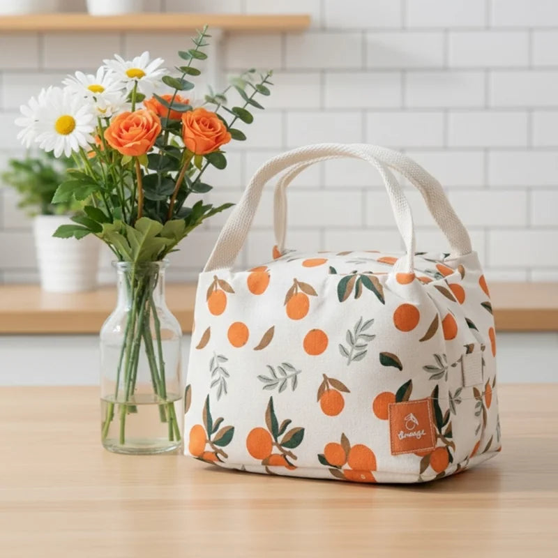 Sac isotherme beige à motifs d’oranges posé sur une table en bois, à côté d’un vase de fleurs colorées.