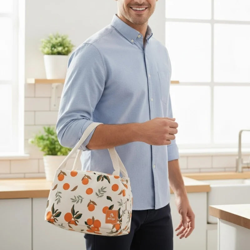 Sac repas isotherme beige à motifs d’oranges porté à la main, idéal pour le bureau ou les repas du midi.