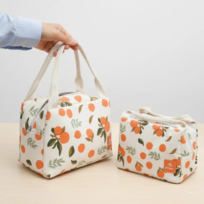 Deux sacs isothermes beige à motifs d’oranges posés sur une table, l’un tenu par une main.