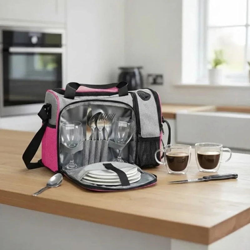Sac isotherme rose et gris ouvert sur un plan de travail, montrant des assiettes, verres et couverts rangés pour un repas organisé.