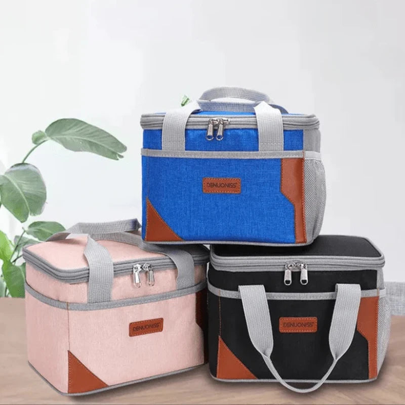 Sacs isothermes repas en trois coloris bleu, rose et noir avec anses grises et détails en cuir synthétique, présentés sur une table intérieure.