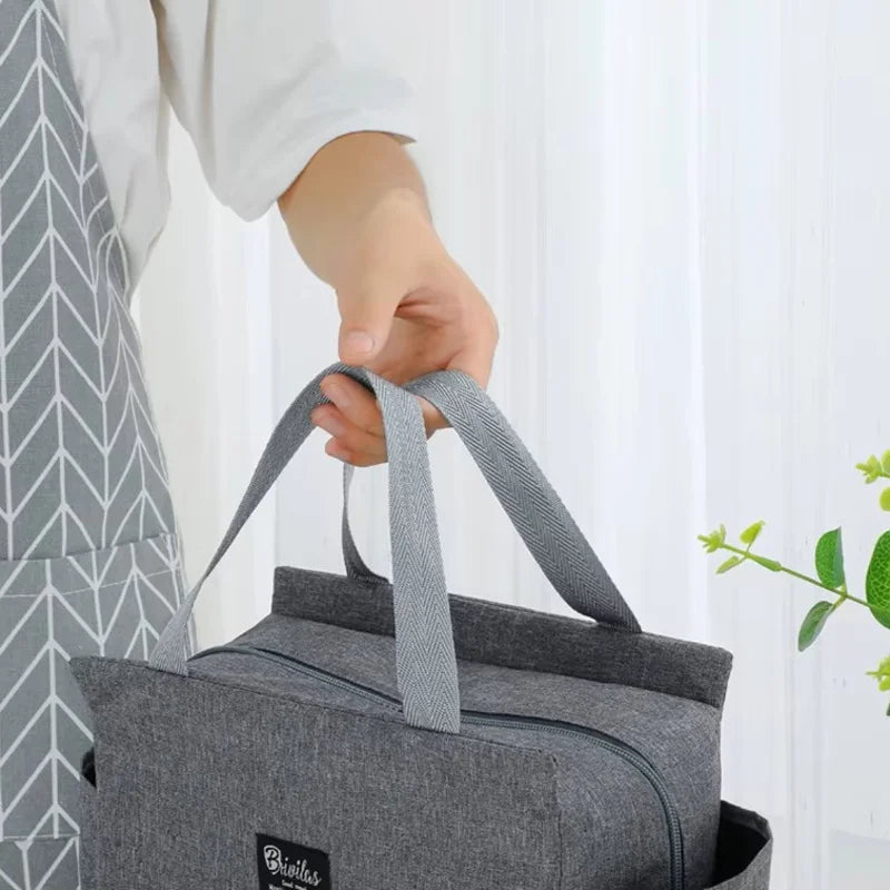 Sac isotherme repas 8L gris tenu à la main par les poignées, avec fermeture zippée sur le dessus, conçu pour transporter un déjeuner ou un repas du midi.