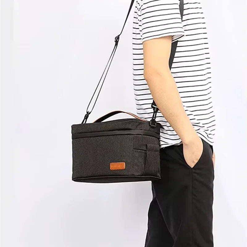 Sac isotherme repas noir porté en bandoulière par un homme, format compact et pratique pour transporter un déjeuner au travail ou en déplacement