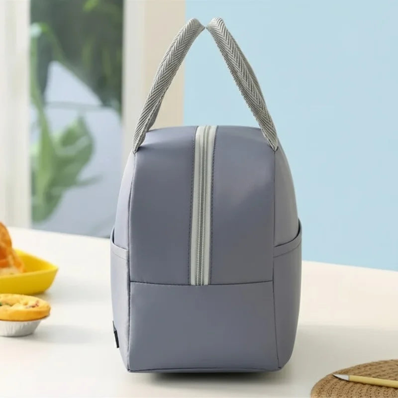 Vue latérale d’un sac isotherme repas bleu posé sur une table, avec fermeture zippée centrale et poignées grises, dans un décor lumineux de cuisine.