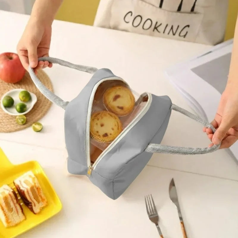 Vue du dessus d’un sac isotherme repas bleu ouvert contenant des pâtisseries, posé sur une table avec des couverts, un gâteau et des fruits.