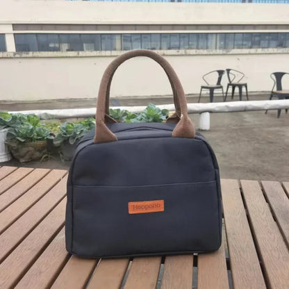 sac isotherme repas bleu marine vu de face, posé sur une table de pique-nique en bois, avec poignées marron et étiquette en cuir