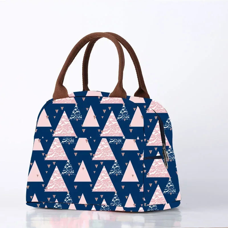 Sac isotherme repas pour femme avec motif géométrique de triangles roses sur fond bleu marine, doté de poignées marron, posé sur une surface claire avec fond blanc épuré.