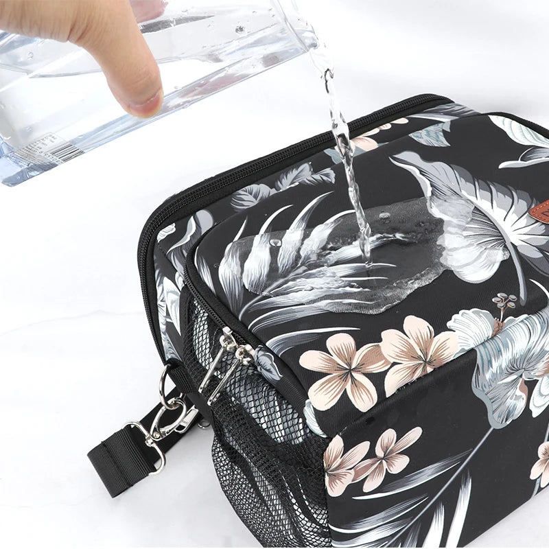Sac isotherme repas femme motif floral noir avec surface déperlante, illustré avec de l’eau versée sur le dessus pour montrer la résistance à l’humidité.