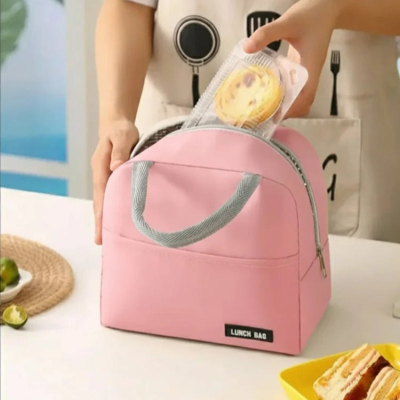 Une personne range un dessert dans un sac isotherme rose clair, posé sur une table blanche avec un sandwich et des citrons verts à côté.