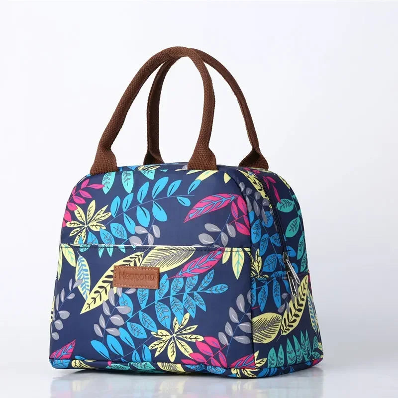 Sac isotherme repas à motifs de feuilles multicolores sur fond blanc, avec anses marron et tissu Oxford imperméable, parfait pour transporter un déjeuner chaud ou froid.